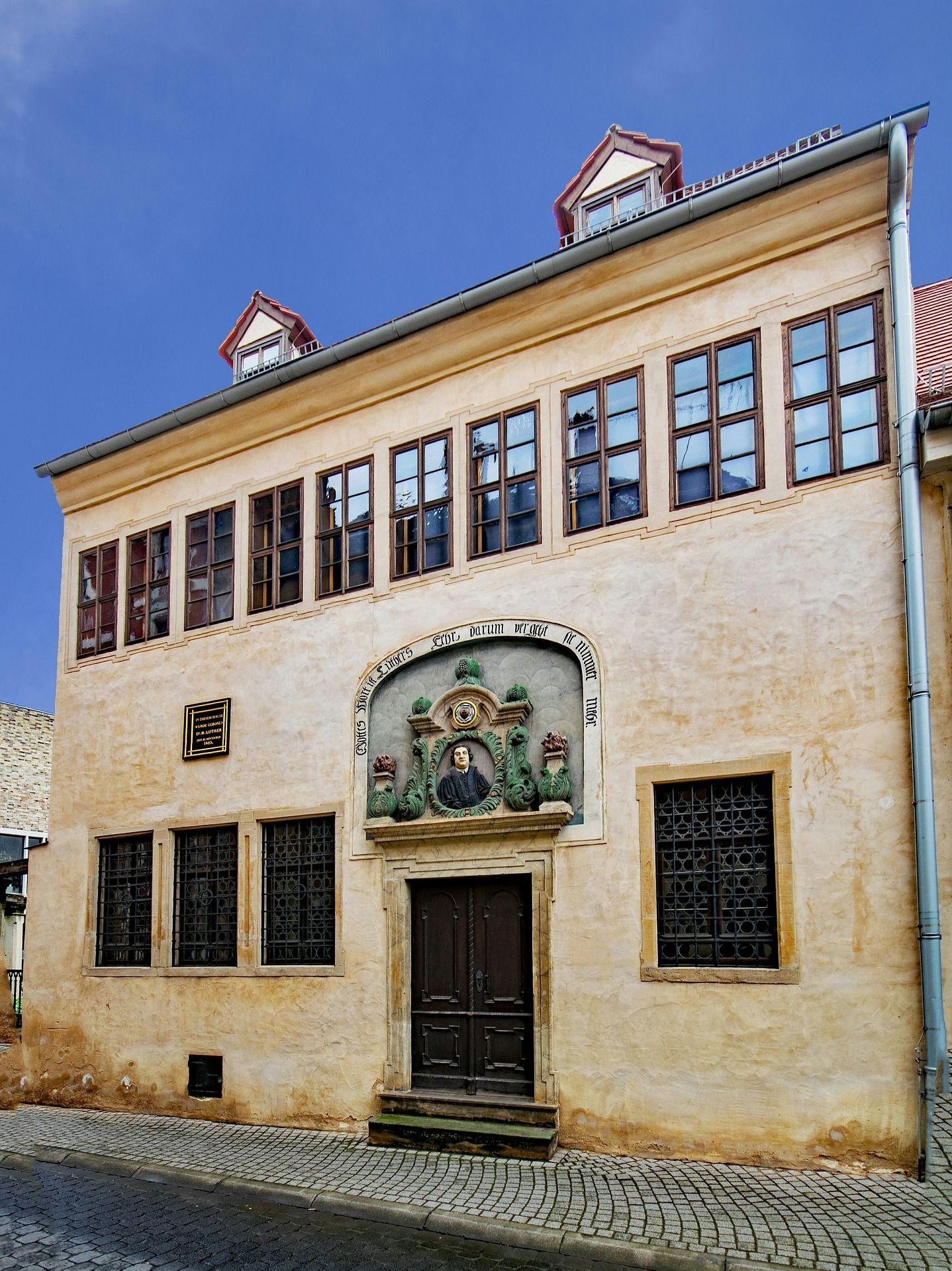 Un bâtiment historique doté d’une entrée imposante, de grandes fenêtres et d’une plaque commémorative.