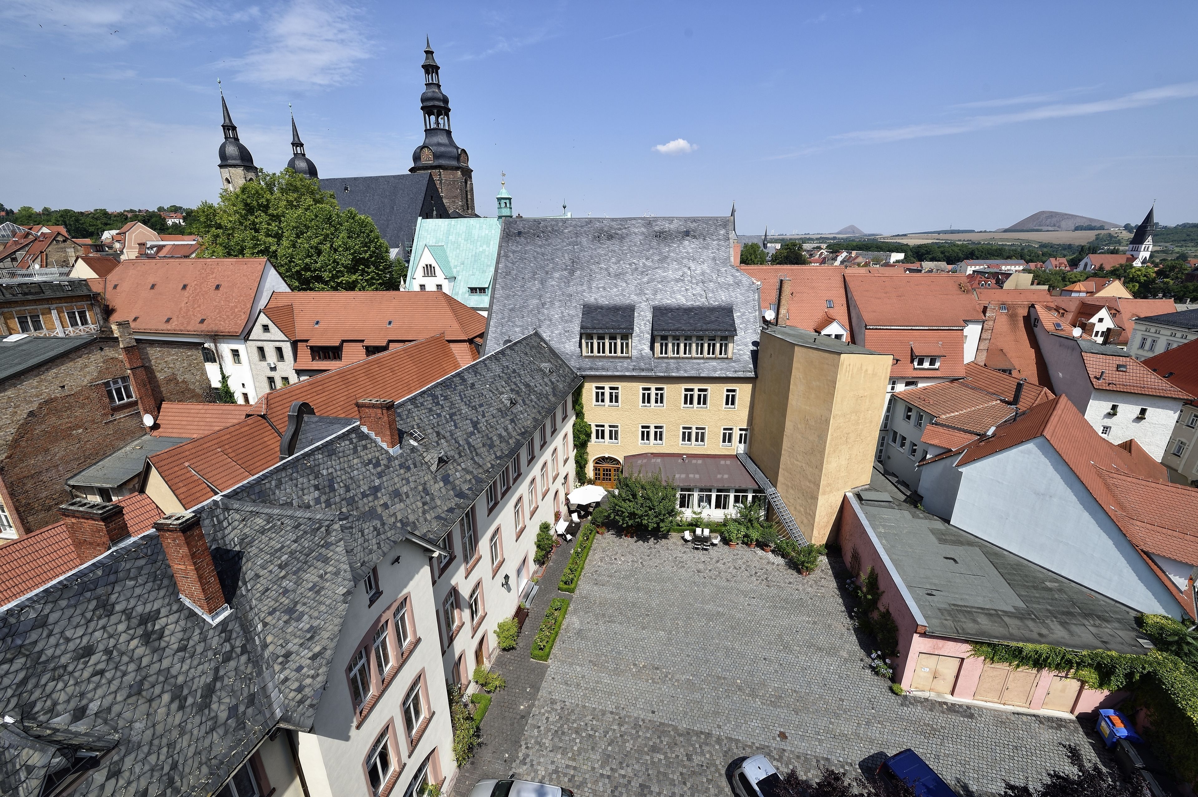 A courtyard surrounded by buildings with red-tiled roofs and a prominent church with two spires in the background.
