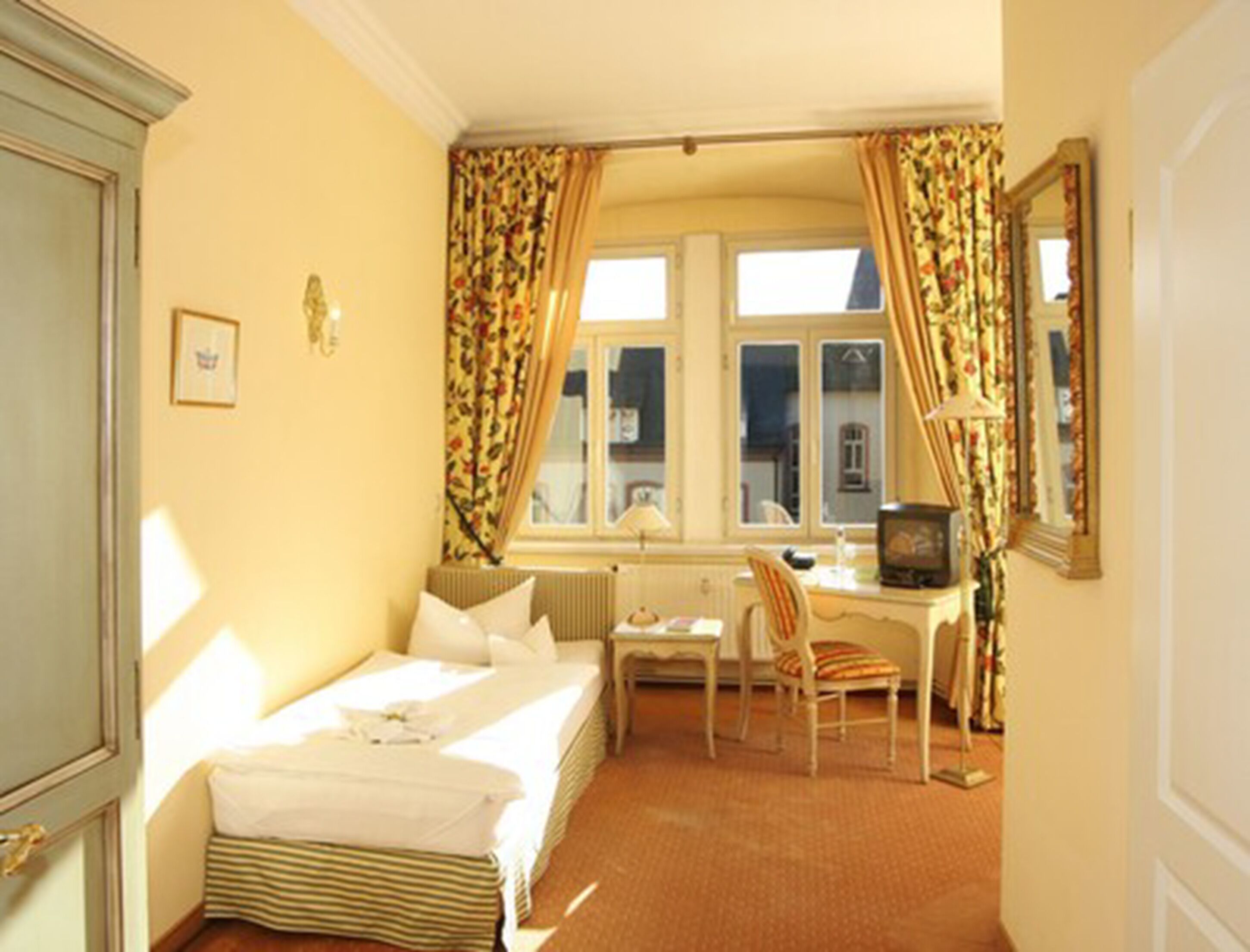 Una camera d'albergo con un letto, una scrivania, una sedia, un termosifone e una televisione.