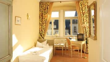 Una camera d'albergo con un letto, una scrivania, una sedia, un termosifone e una televisione.