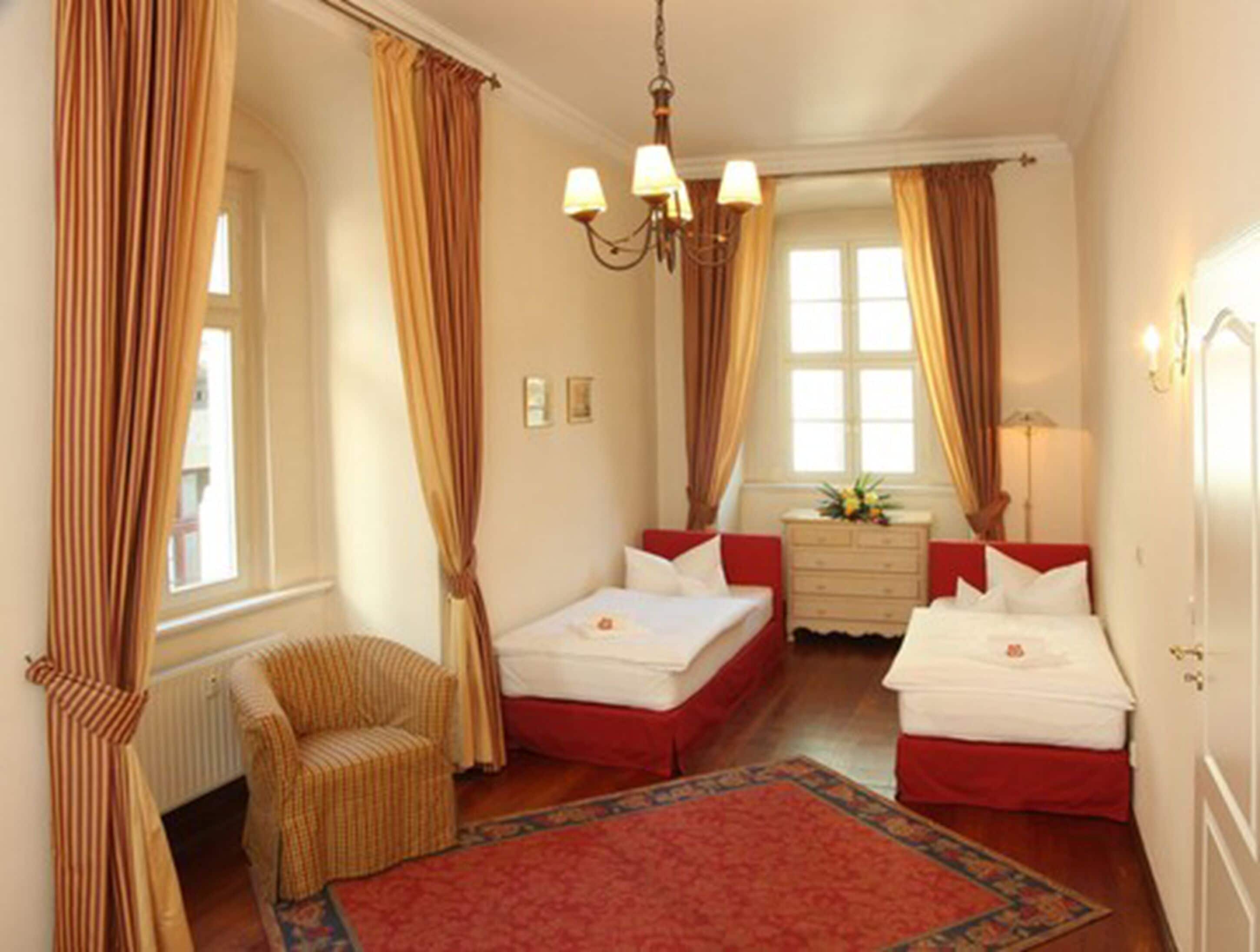 A hotel room with two beds, a chair, a dresser, and a large window with curtains.