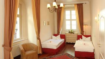 A hotel room with two beds, a chair, a dresser, and a large window with curtains.