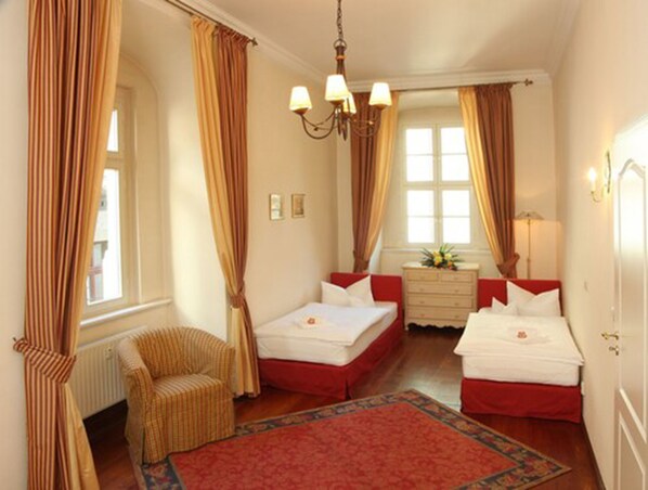 A hotel room with two beds, a chair, a dresser, and a large window with curtains. - Hotel Graf von Mansfeld (Lutherstadt Eisleben)