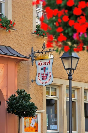 A hotel sign with a coat of arms, a window with a poster, and a street lamp.