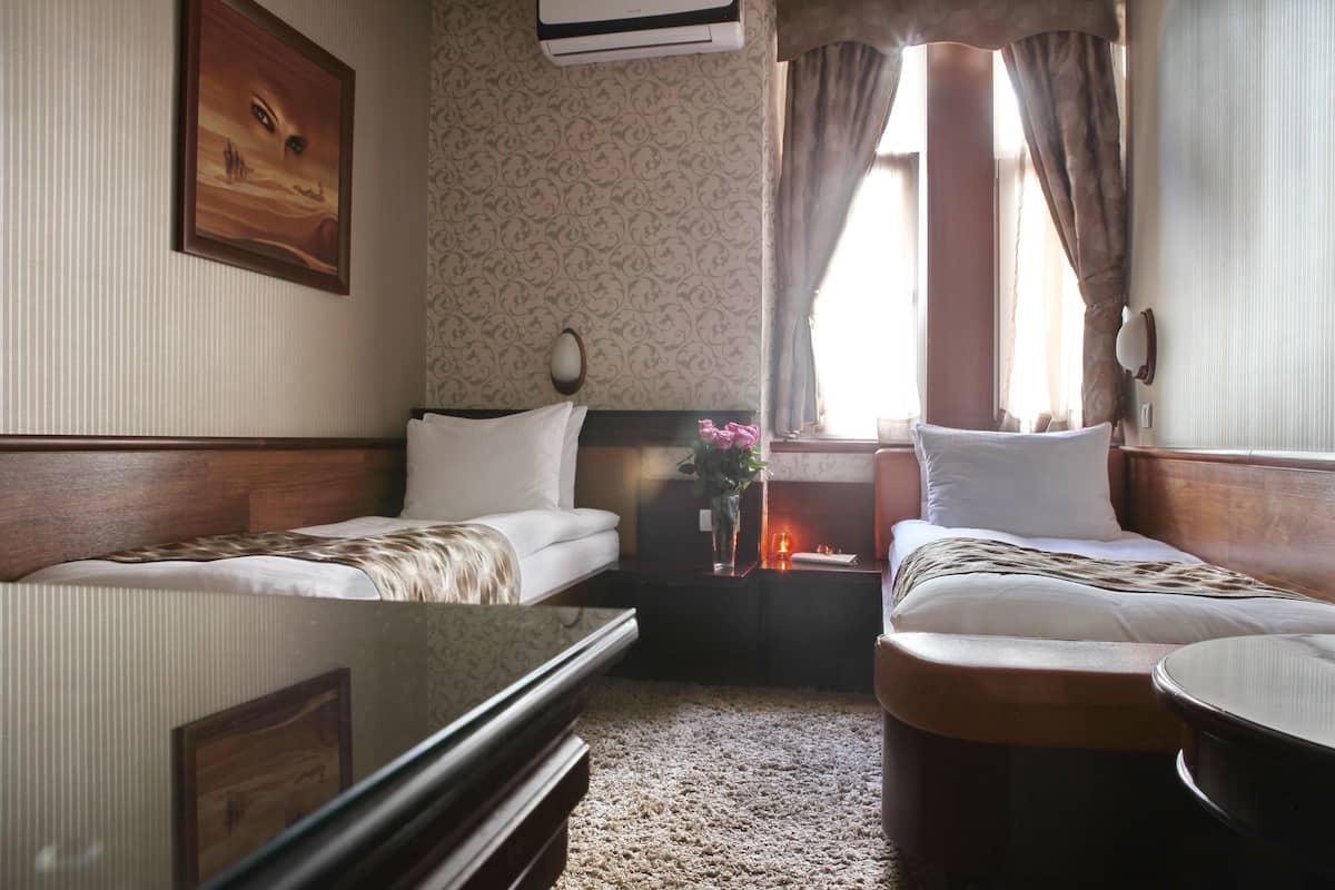 Habitación de hotel con dos camas individuales, una mesita, un espejo y una ventana con cortinas.
