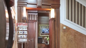 Un pasillo con una puerta de madera, una silla, una mesa redonda y un objeto verde, además de un cartel con tarjetas.