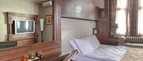 A hotel room with a bed, a desk with a glass top, a television, and a mirror.