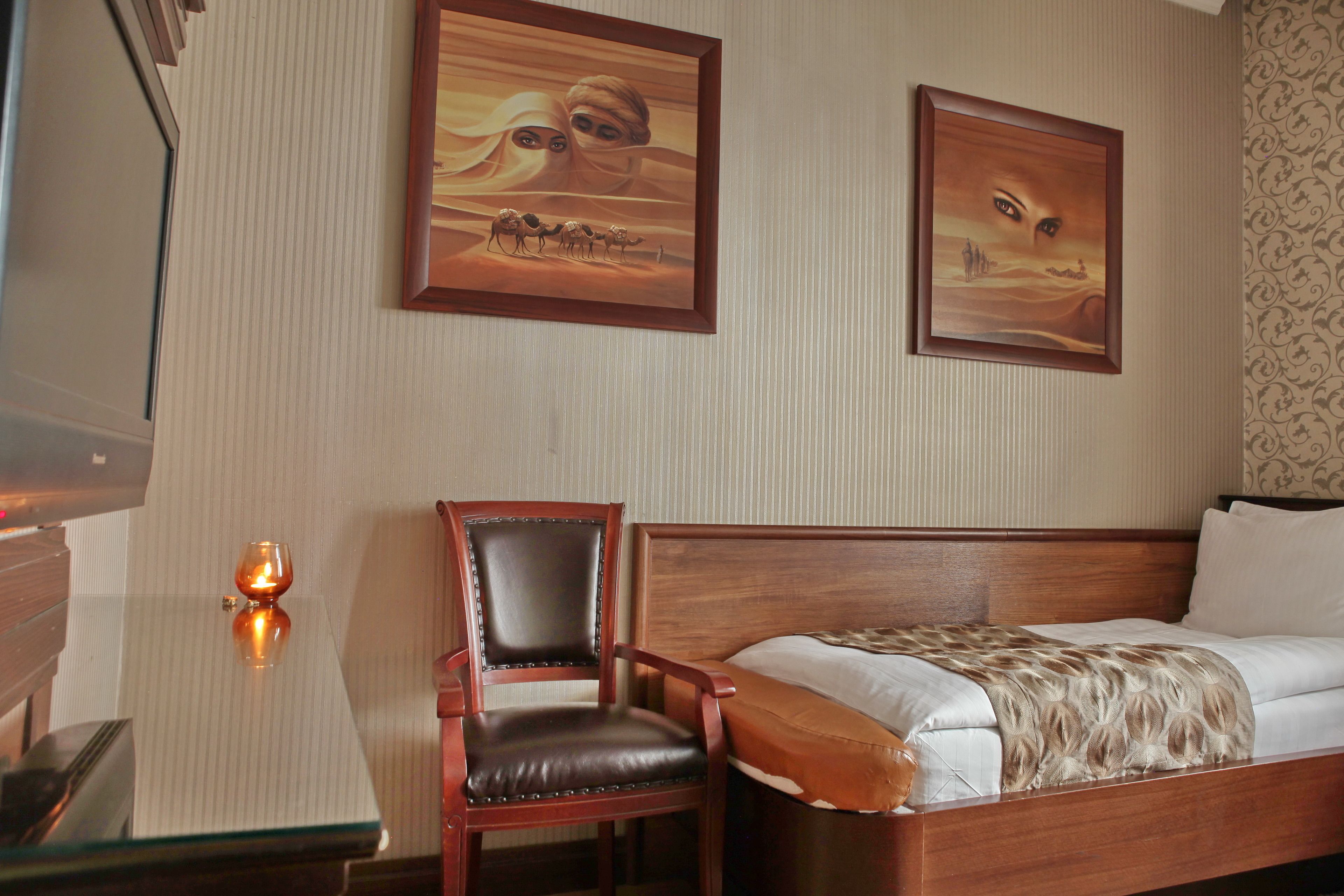 Una habitación de hotel con una cama de madera, una silla, una mesa y dos cuadros en la pared.