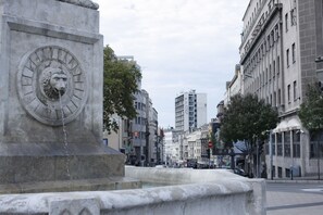 A stone fountain with a lion's head and water spouting from its mouth, set in a city square with buildings around. - Vila Terazije (Belgrade)