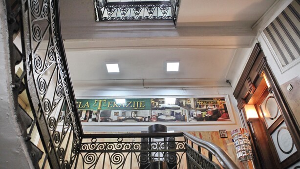 Una escalera con barandillas de metal ornamentadas y un área de recepción al fondo.