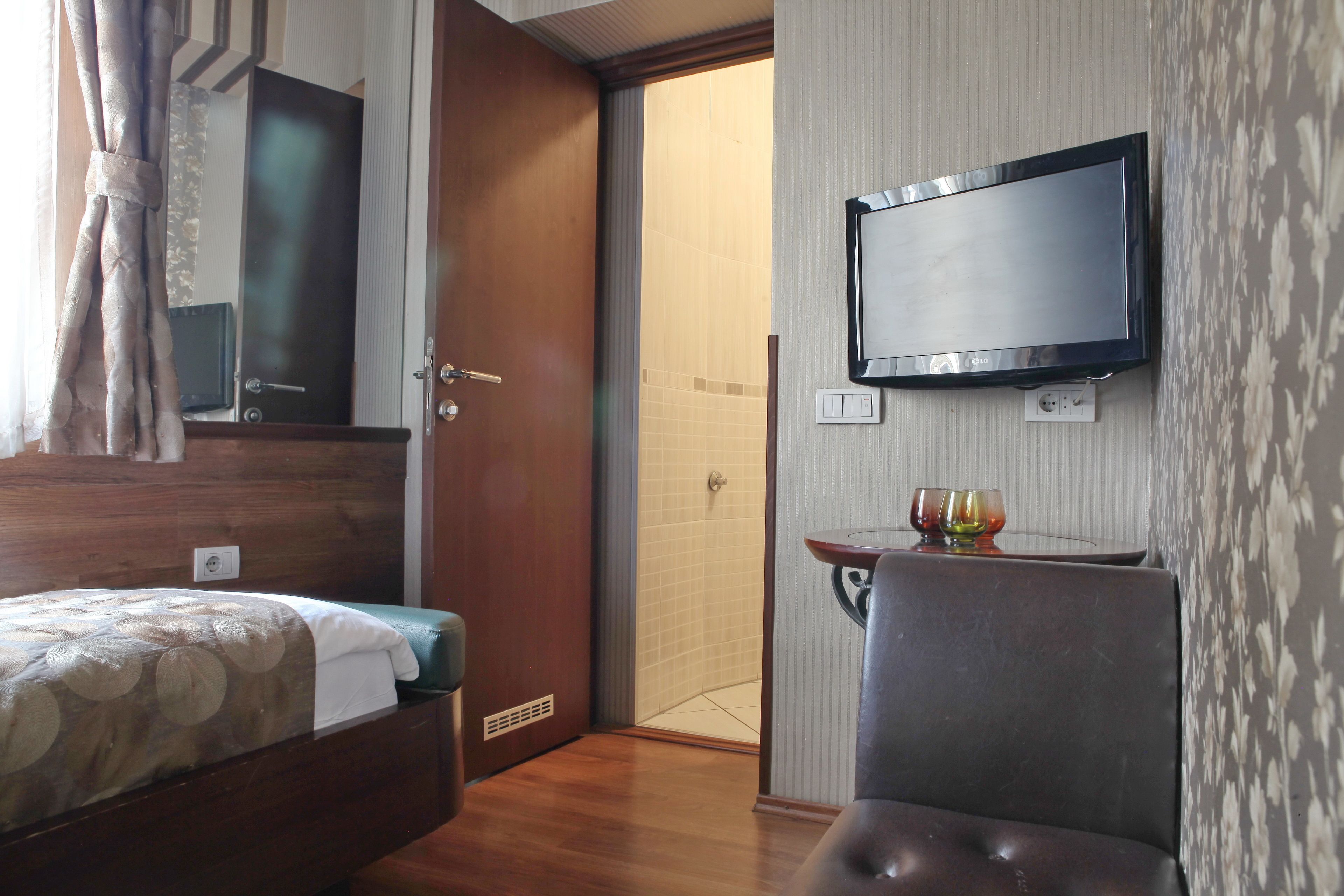 A hotel room with a bed, a television mounted on the wall, a small table with a glass, and a shower area.