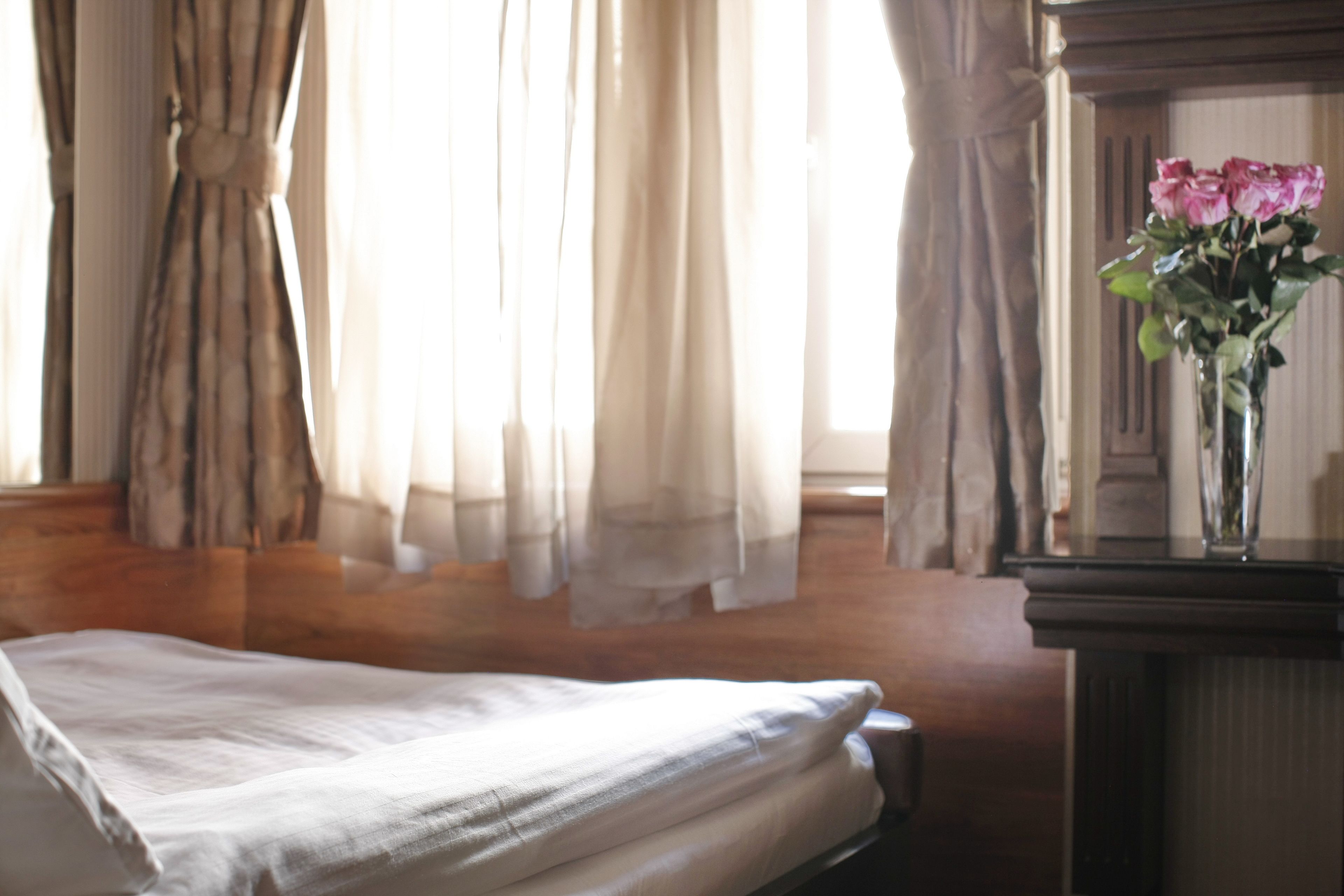 Quarto com cama, vaso de flores e cortinas.