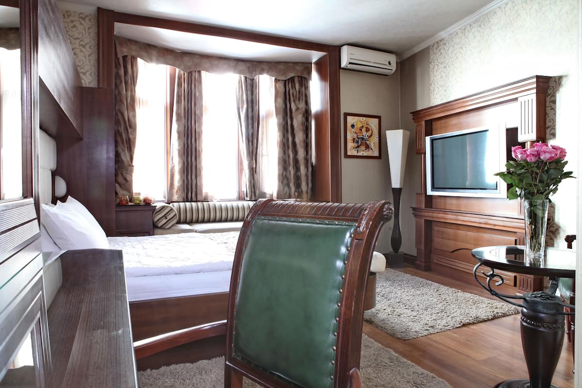 Habitación de hotel con cama, escritorio, silla, televisor y un florero con flores.