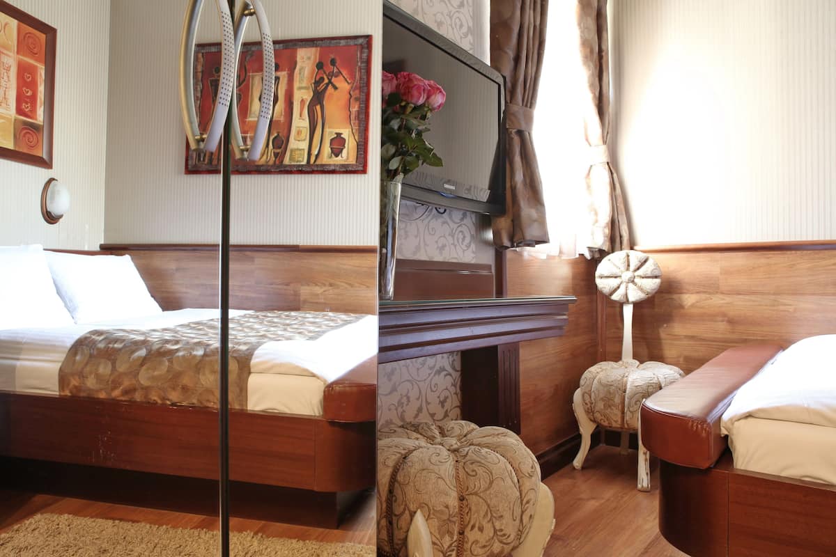 Habitación de hotel con una cama de madera, un televisor, una lámpara decorativa y un taburete pequeño.