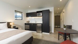 Habitació d'hotel moderna amb un llit gran, una cuineta petita, zona de menjador i un bany.