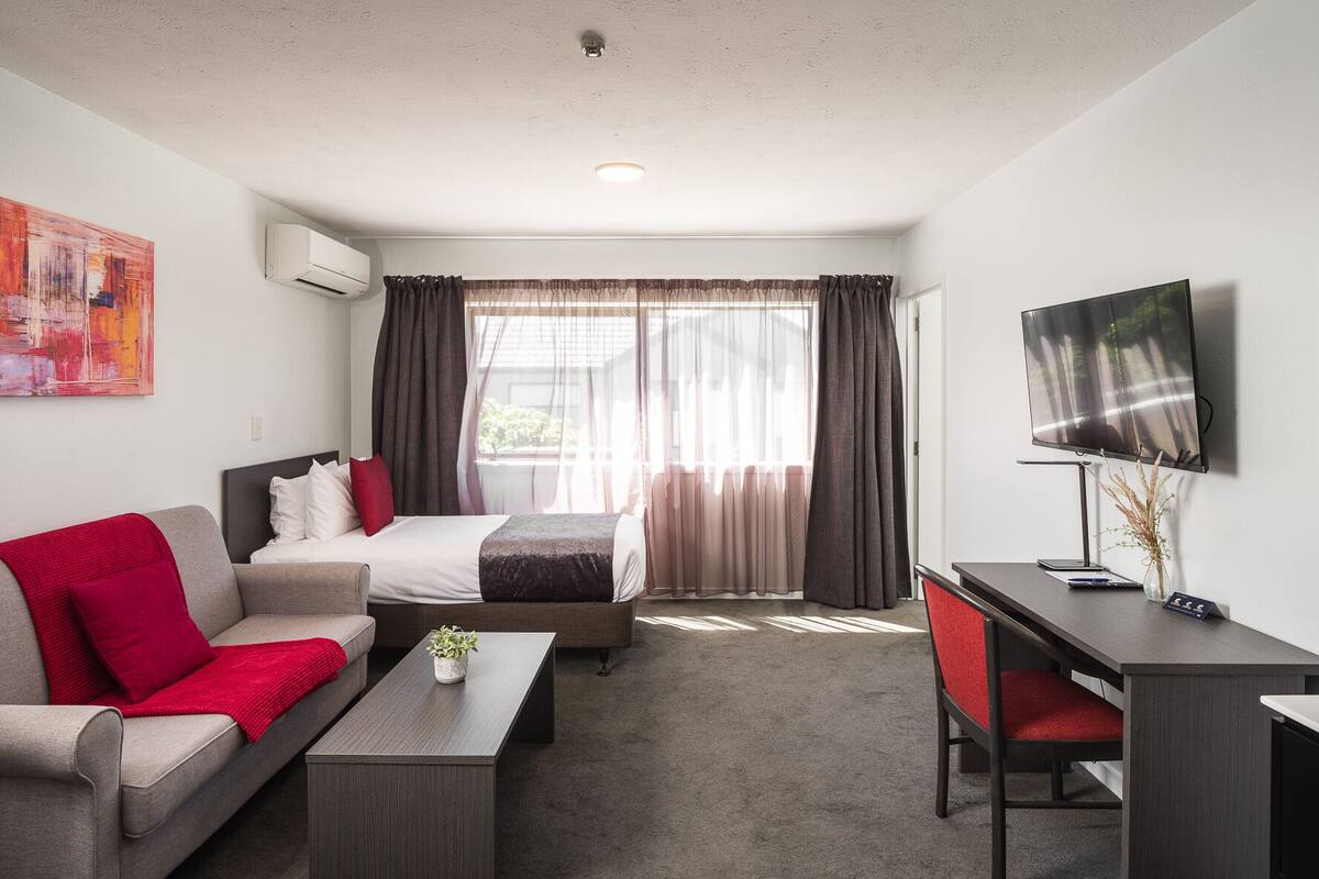 Moderni hotellihuone, jossa on sänky, sohva, työpöytä ja televisio.