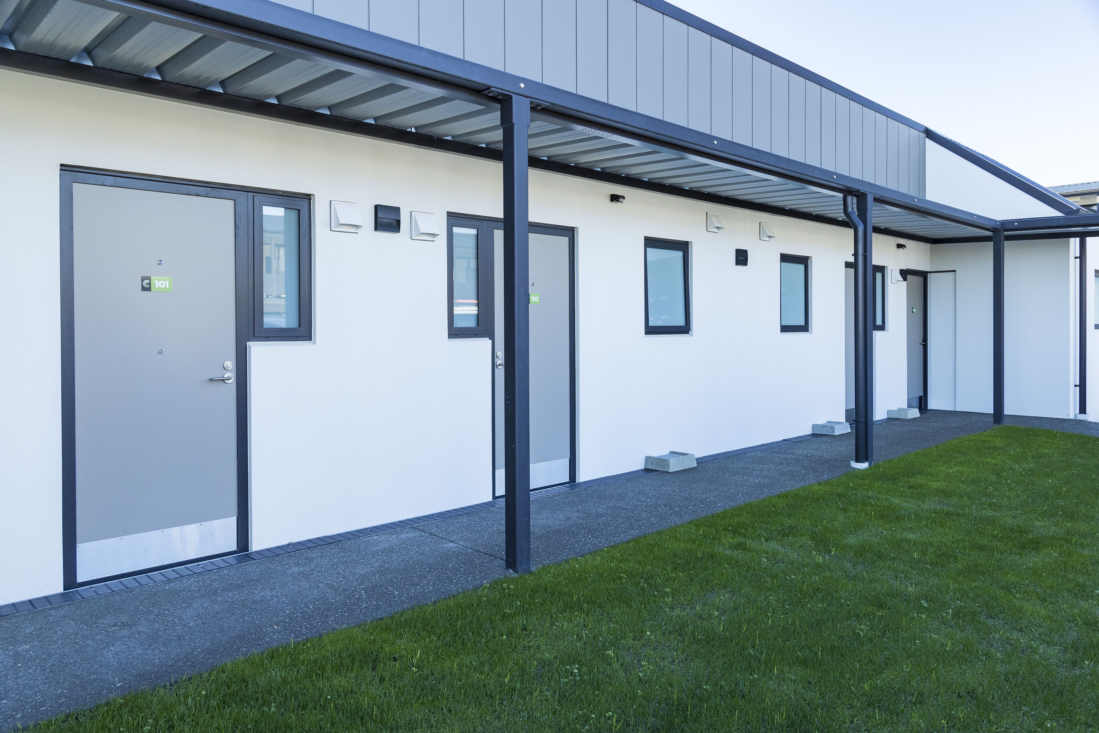 A modern building with a covered walkway, multiple doors, and a well-maintained lawn.