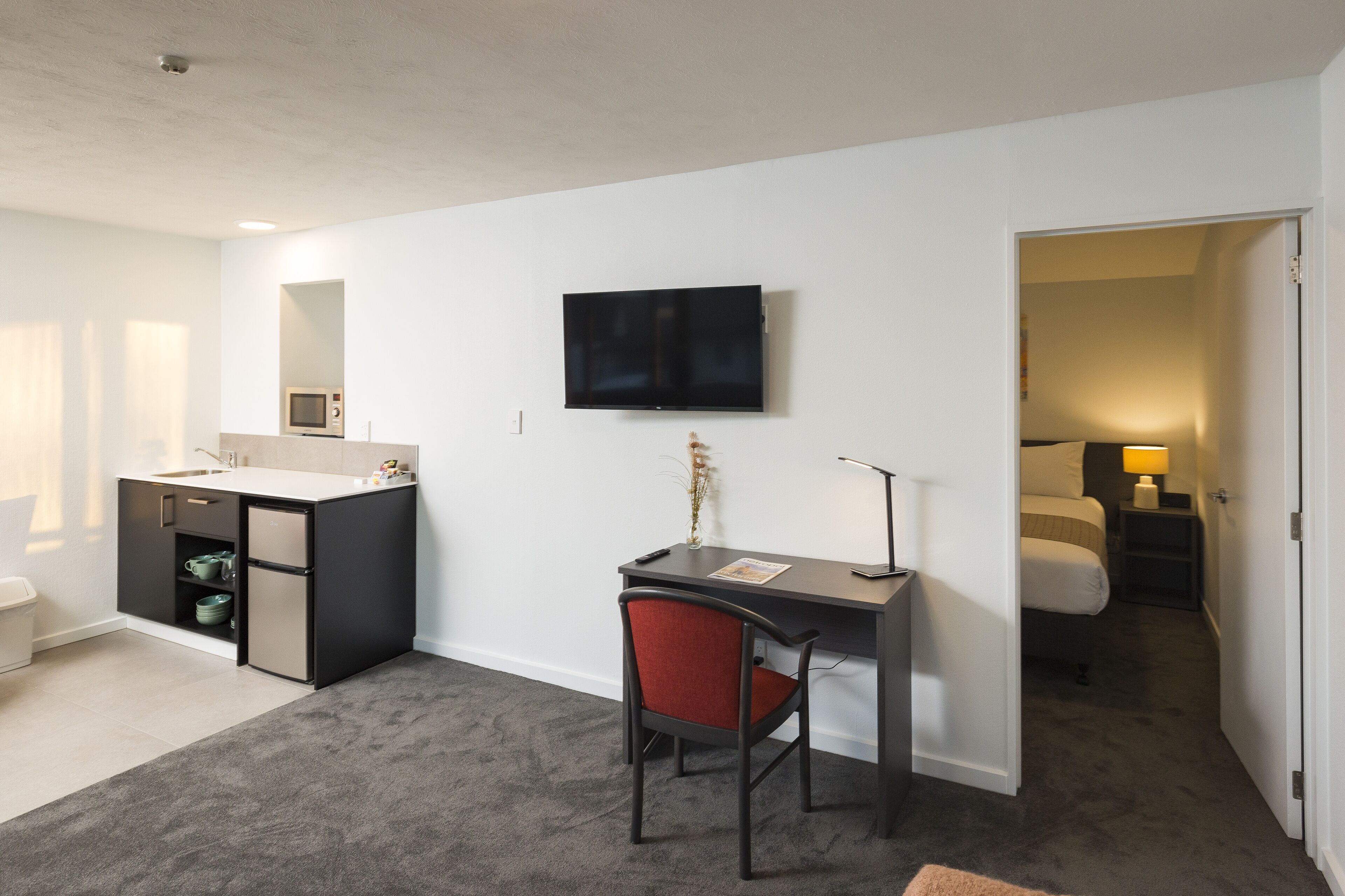 Habitación de hotel compacta con kitchenette, un escritorio con silla, televisor de pantalla plana y cama.