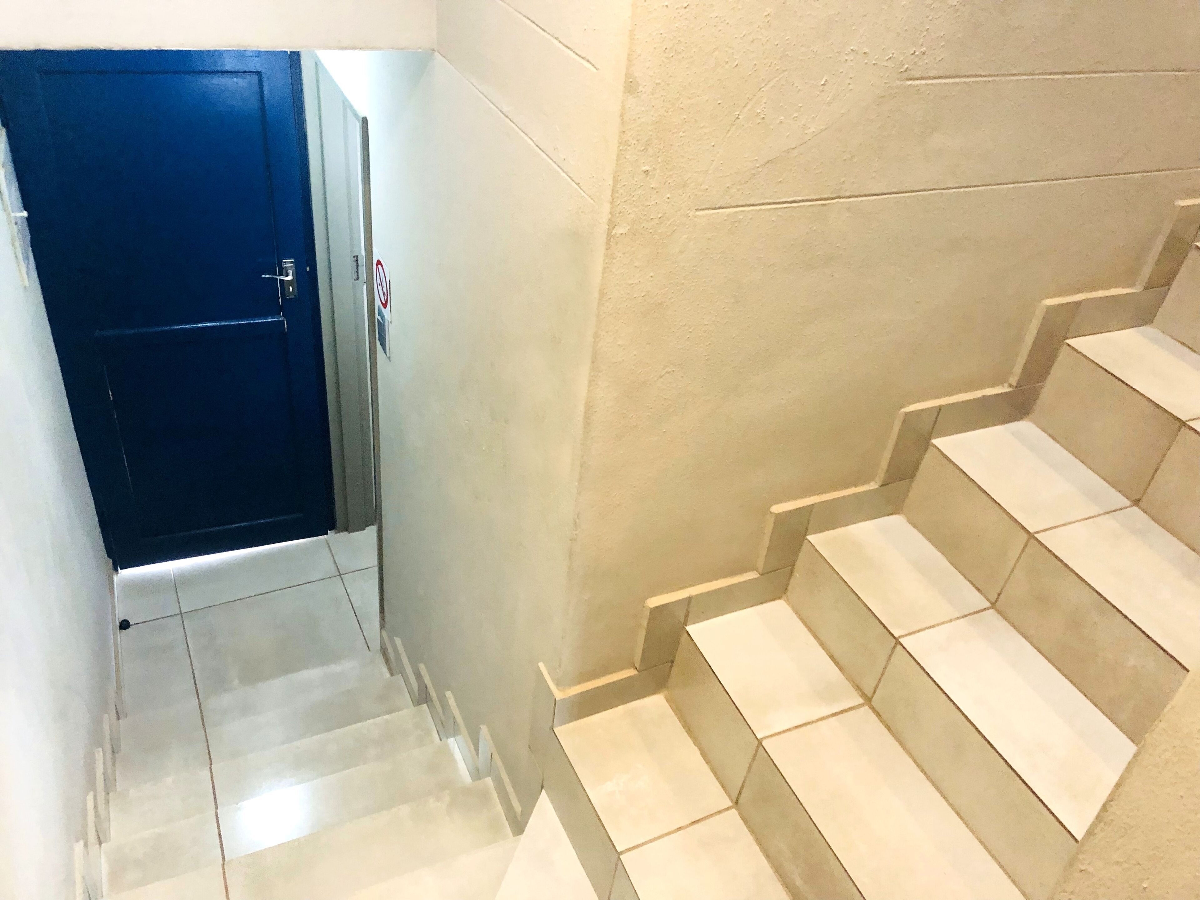 A staircase with beige tiles and a blue door at the top.