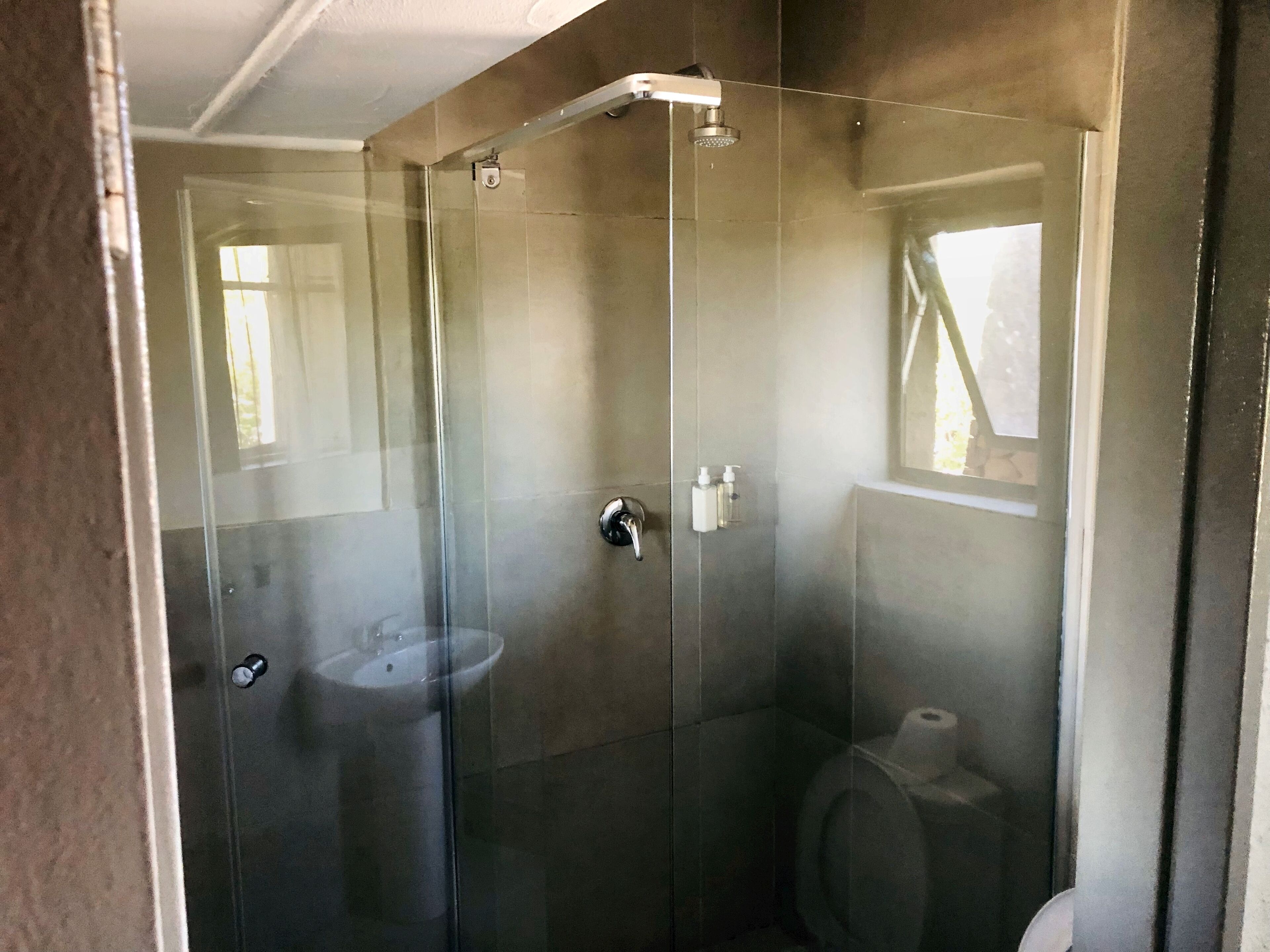 Ducha con cerramiento de vidrio, inodoro y lavamanos.