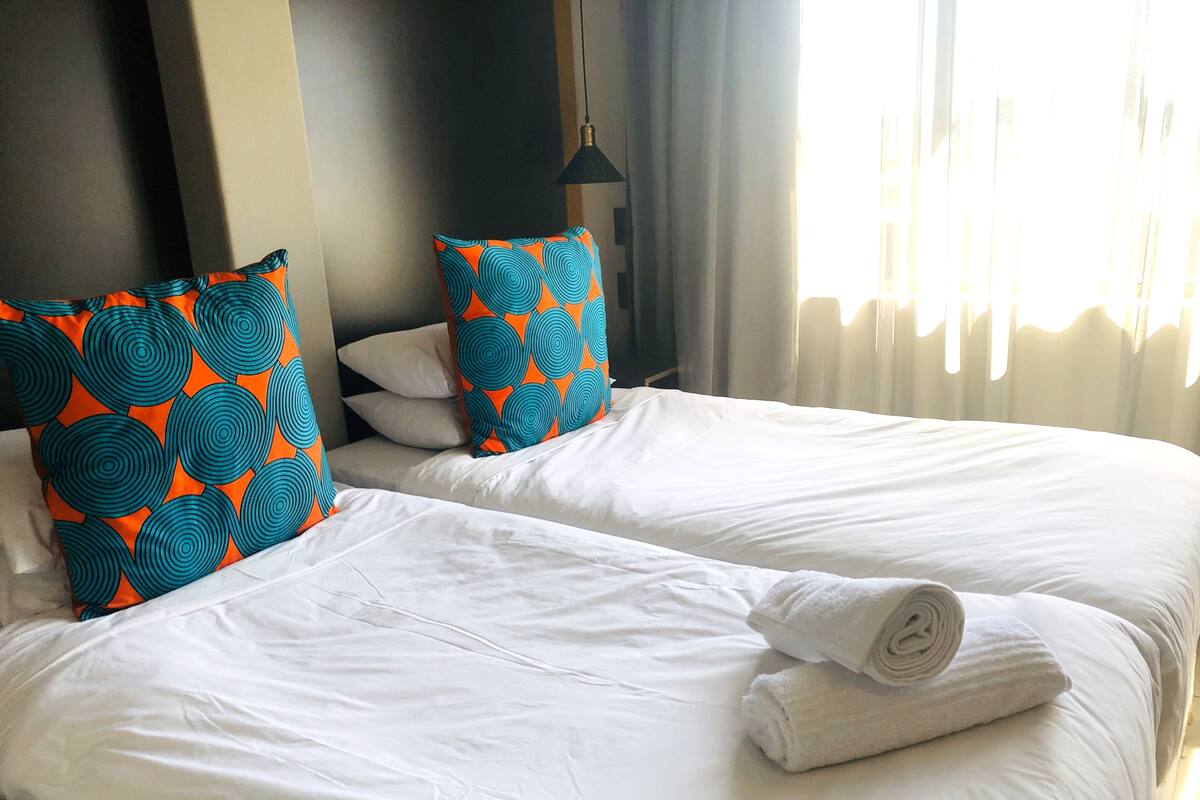 Une chambre d’hôtel avec deux lits, du linge de lit blanc et des oreillers à motifs orange et bleu.