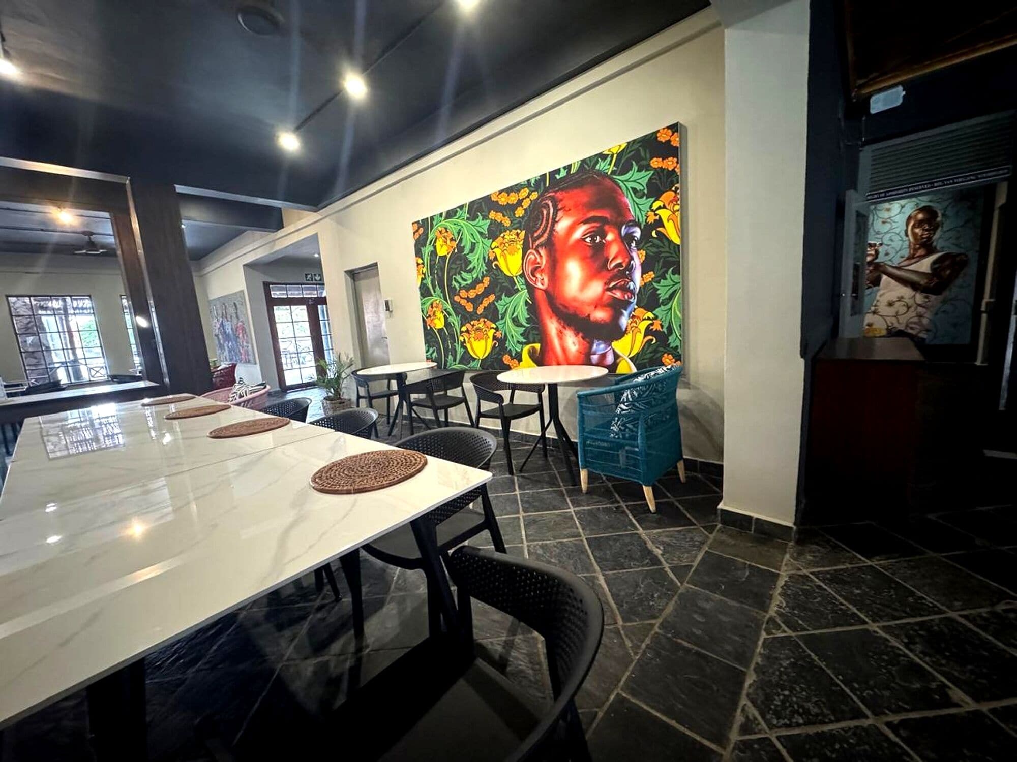 Un comedor moderno con un amplio mural, pisos de baldosas blanco y negro y diferentes opciones de asientos, incluyendo mesas redondas y sillas.