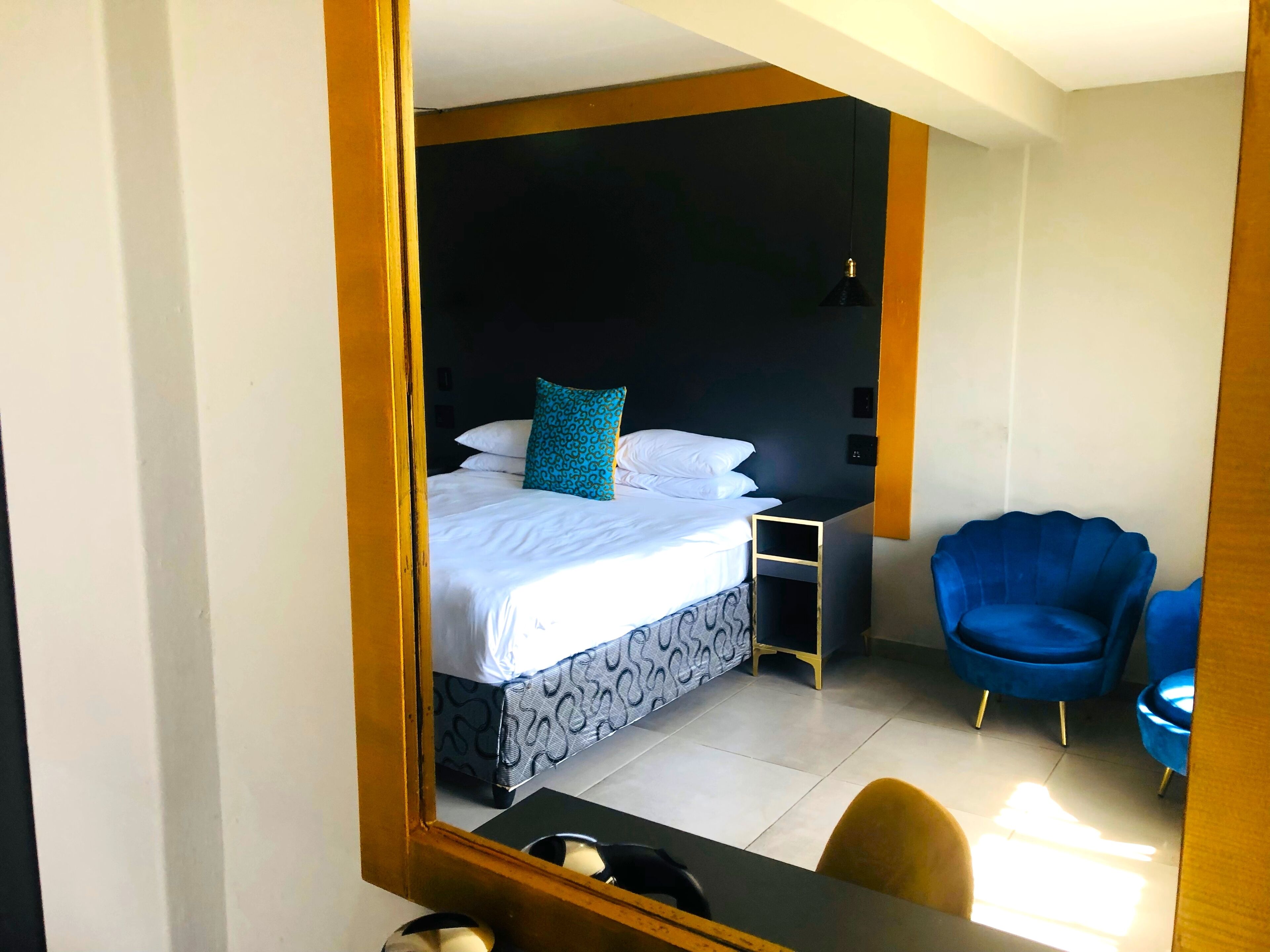 Quarto de hotel com cama, escrivaninha e duas cadeiras azuis.