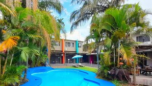 Une piscine entourée de palmiers et un bâtiment doté d’un patio couvert.