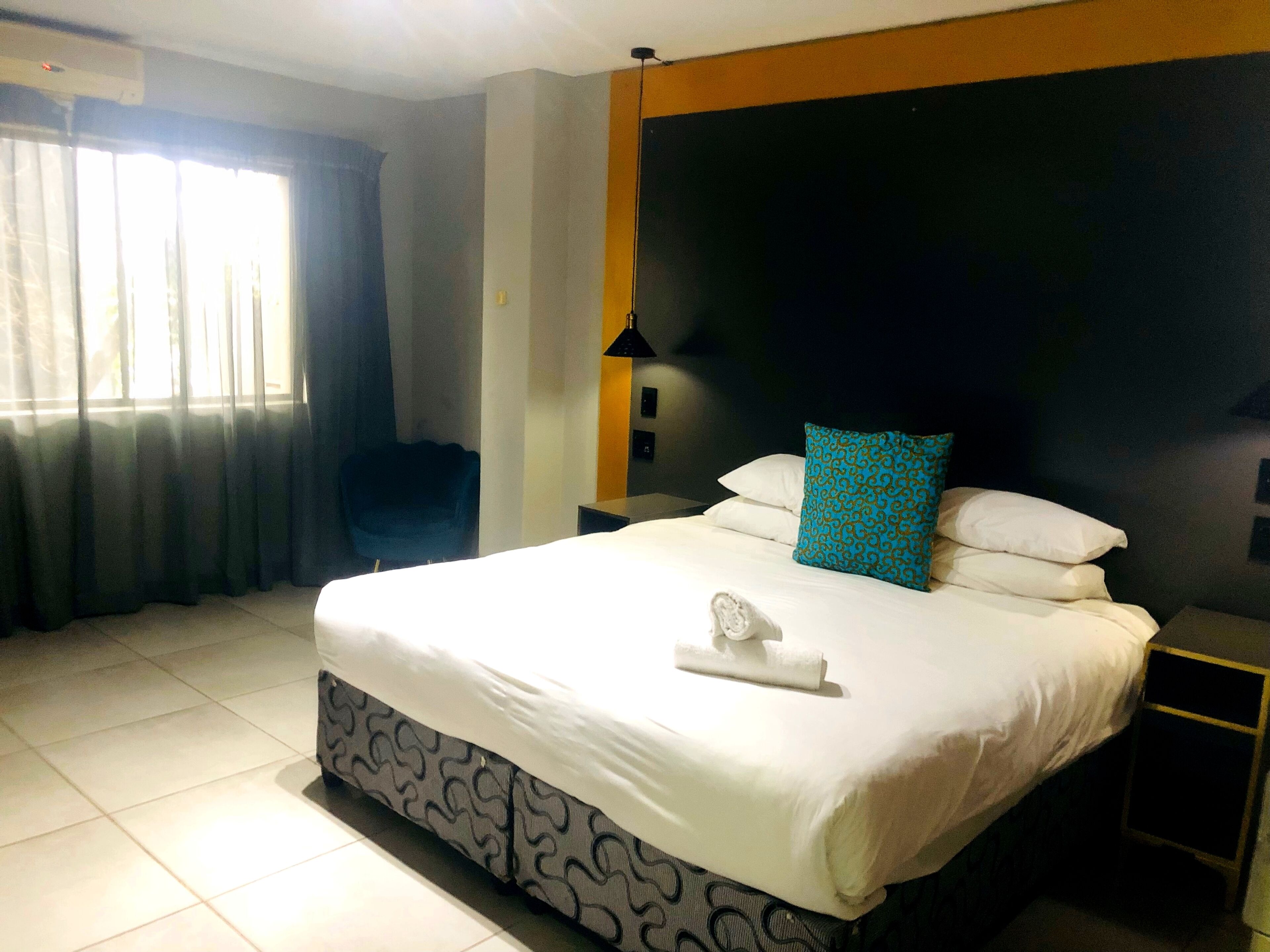 Habitación de hotel con una cama grande, una silla, una mesita de noche y un ventanal con cortinas.