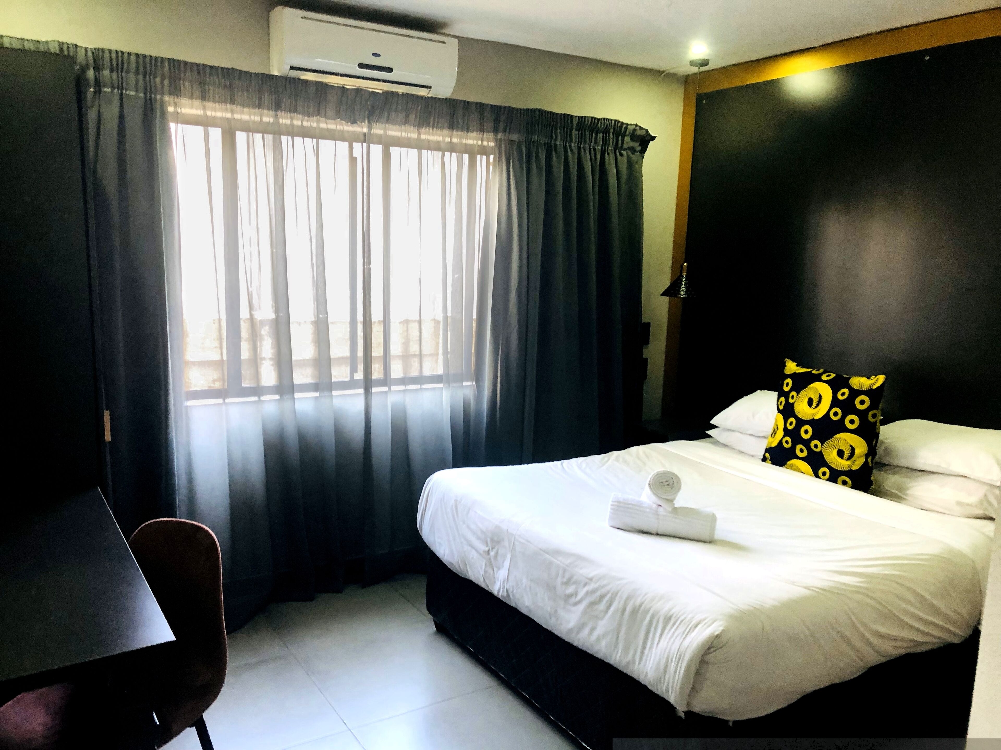 A hotel room with a bed, a chair, a desk, and a window with curtains.