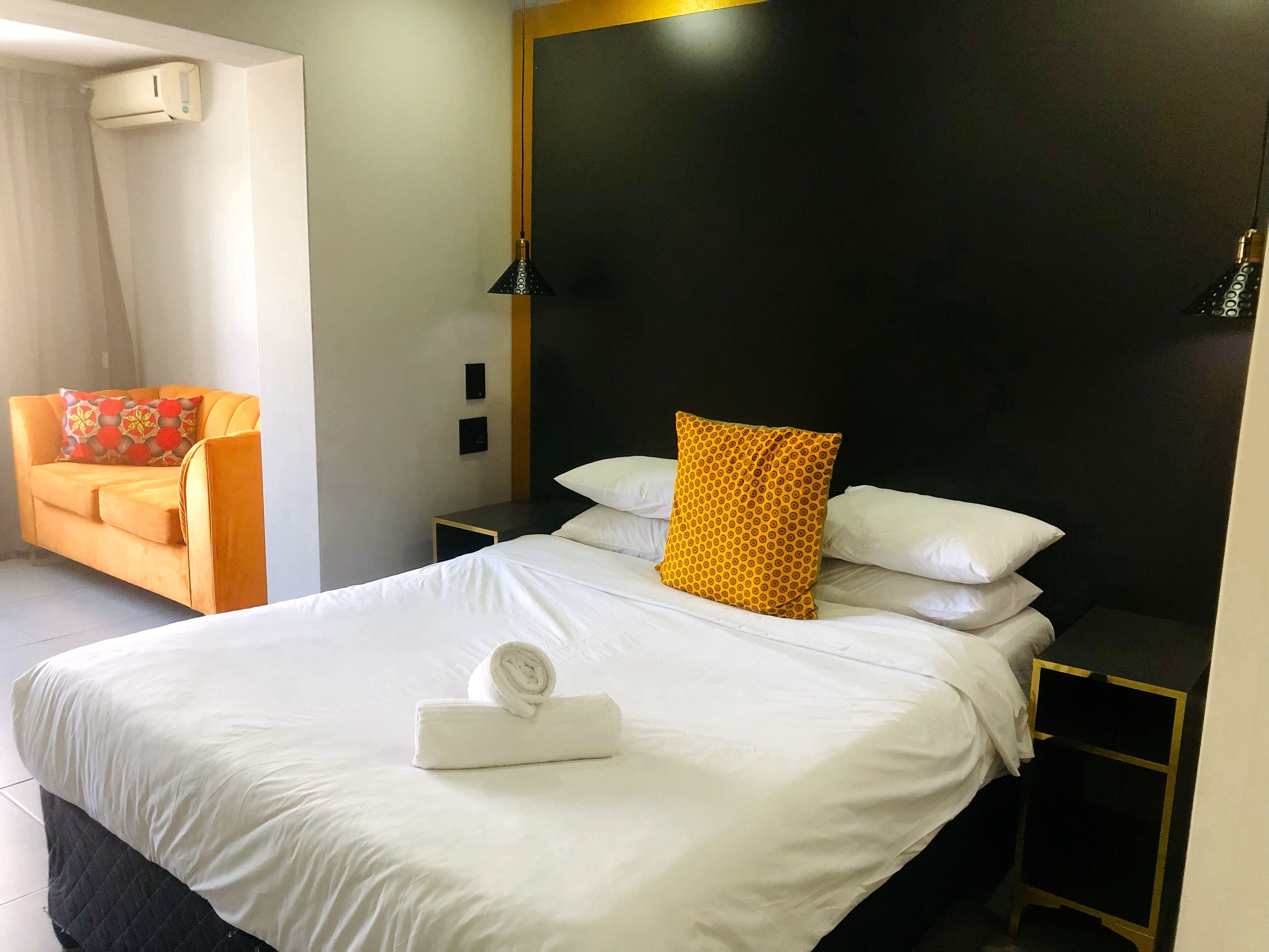A hotel room with a bed, a nightstand, a chair, and a wall-mounted air conditioner.