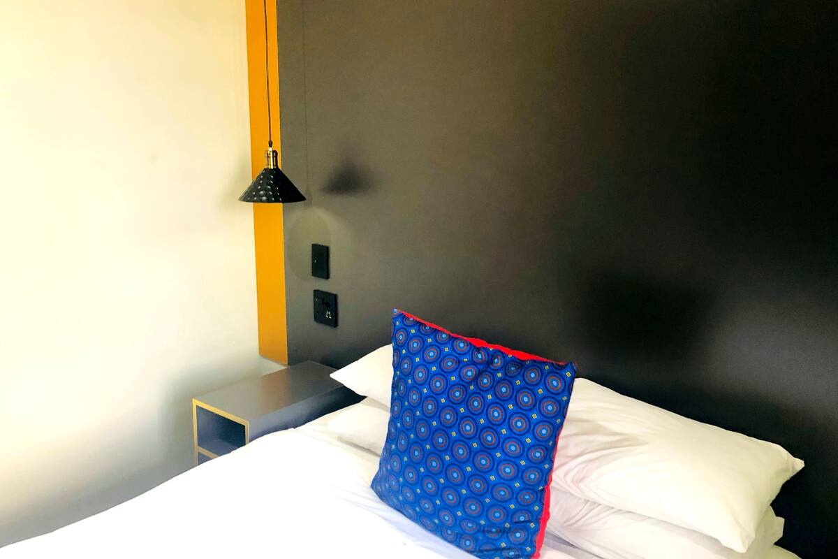 Une chambre d’hôtel avec un lit, une table de chevet, une lampe et un mur muni d’un interrupteur.