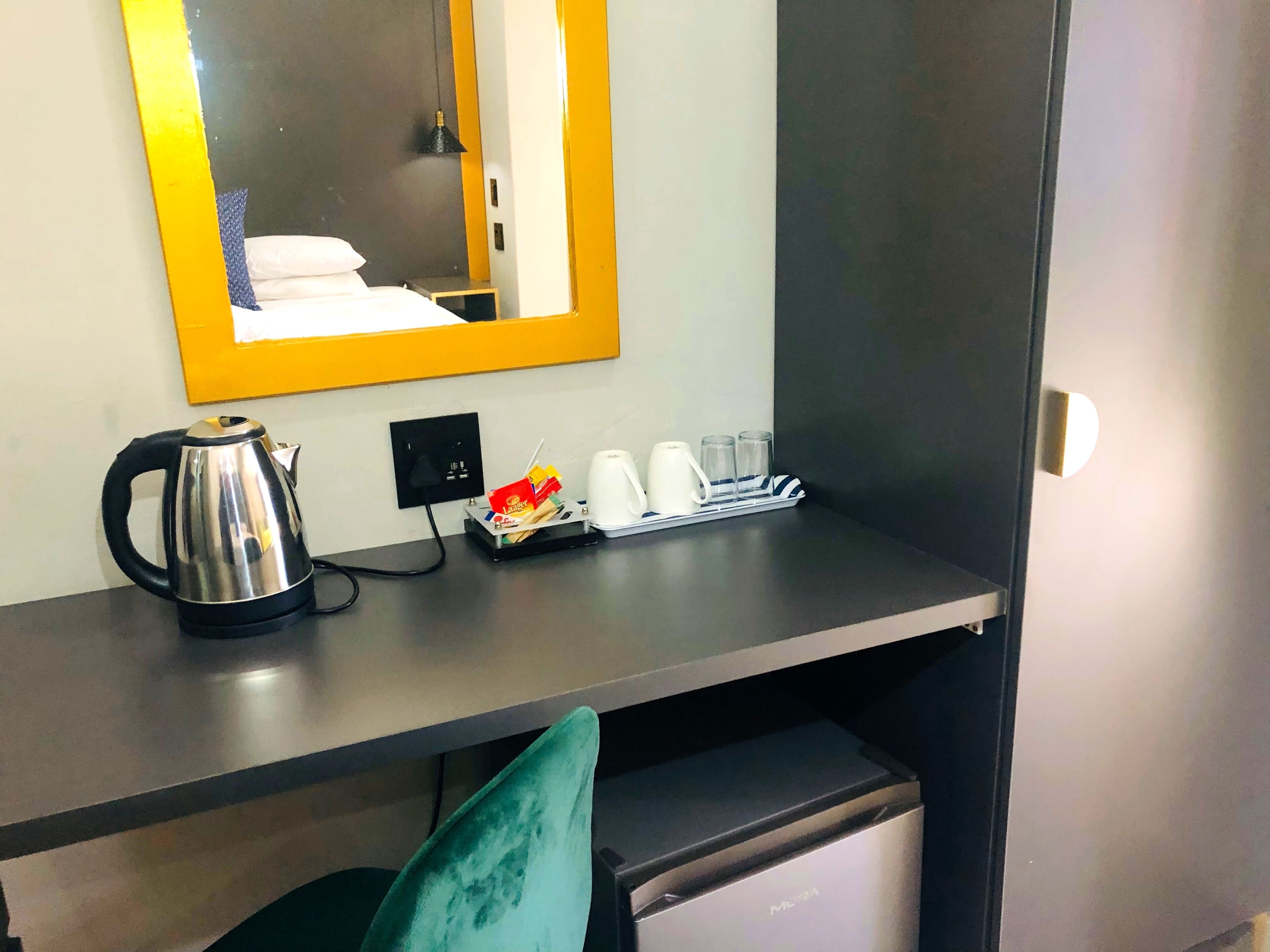A hotel room with a desk, a kettle, a coffee maker, and a tray with cups and glasses.