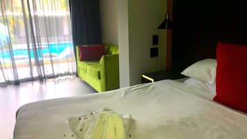 A hotel room with a bed, a green armchair, a red pillow, and a view of a swimming pool through sheer curtains.