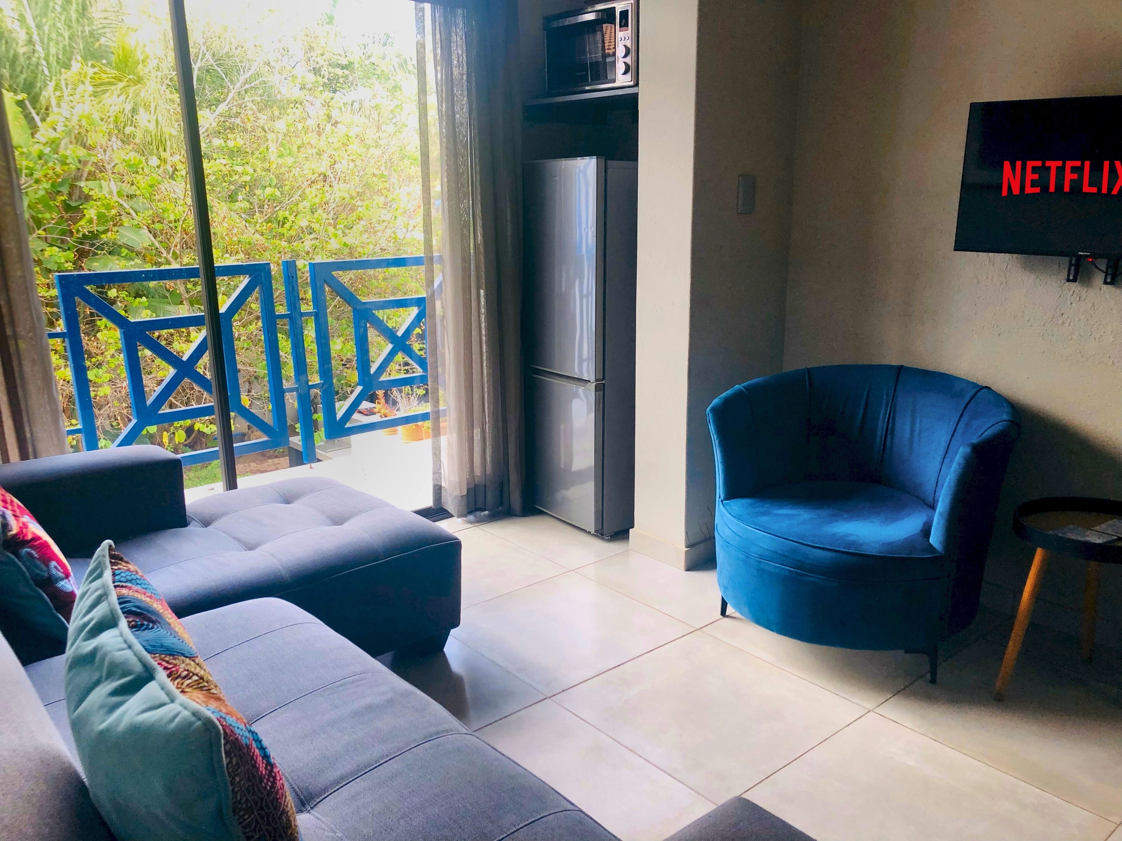 A modern living room with a grey sofa, a blue armchair, and a flat-screen TV mounted on the wall.