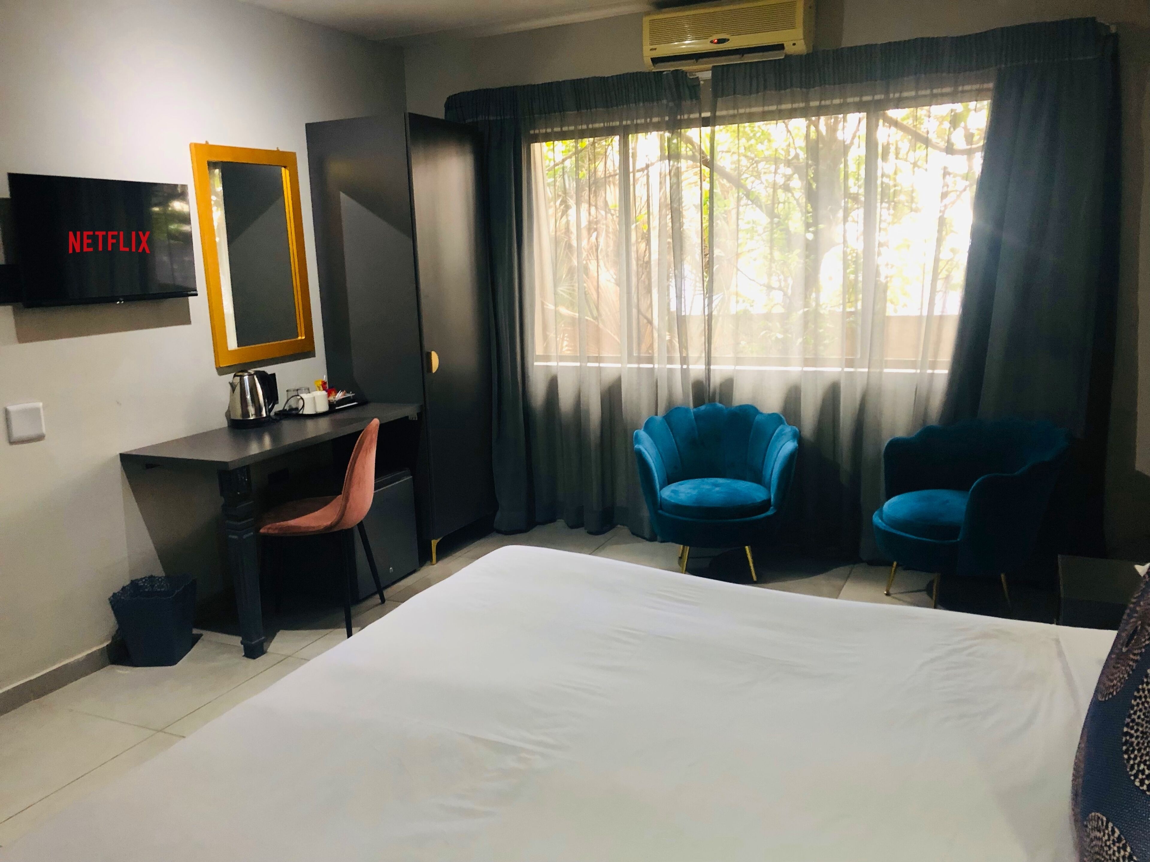 Habitación de hotel con una cama, un escritorio con una silla, un televisor y dos sillas azules.