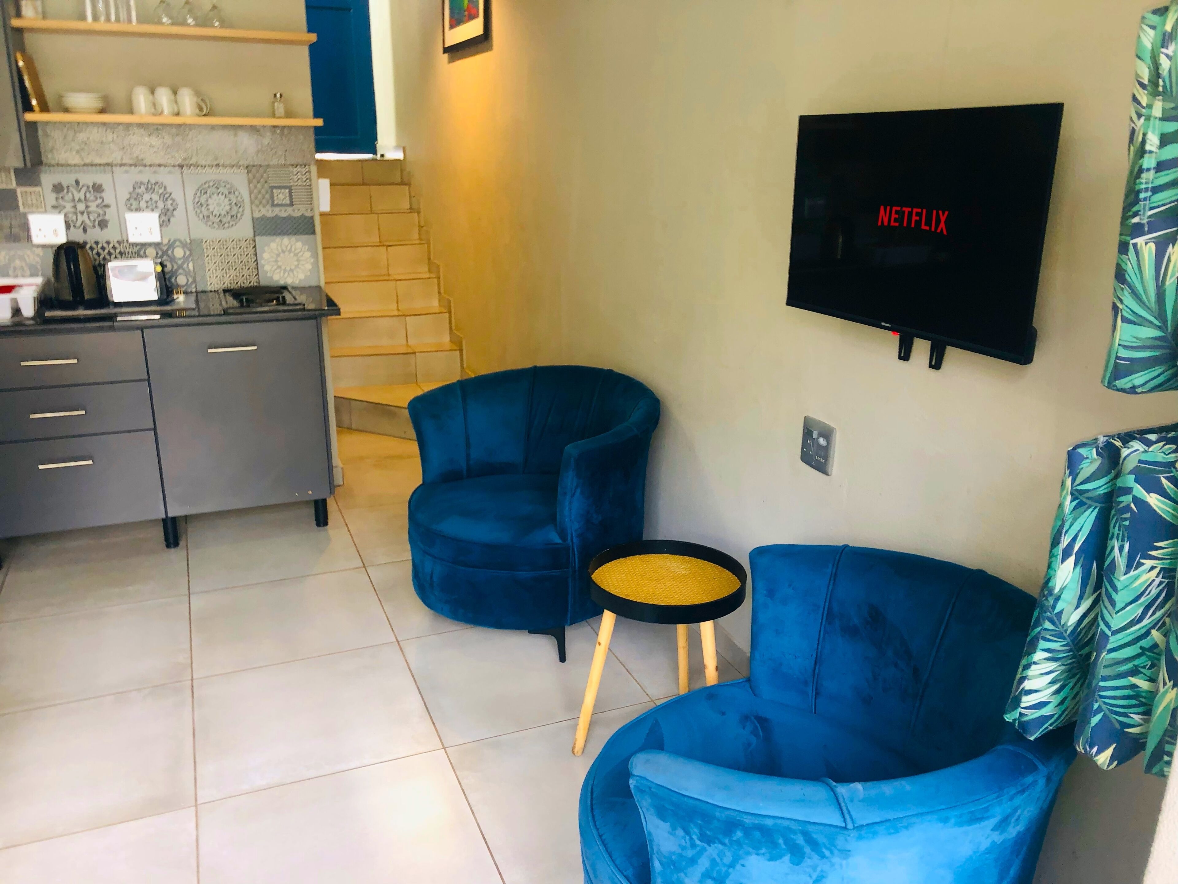 Un espace de vie moderne comprenant une cuisine, deux fauteuils bleus, une petite table ronde et un téléviseur fixé au mur qui affiche le logo de Netflix.