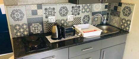 Uma cozinha com azulejos estampados, uma cafeteira, uma torradeira e uma pia.