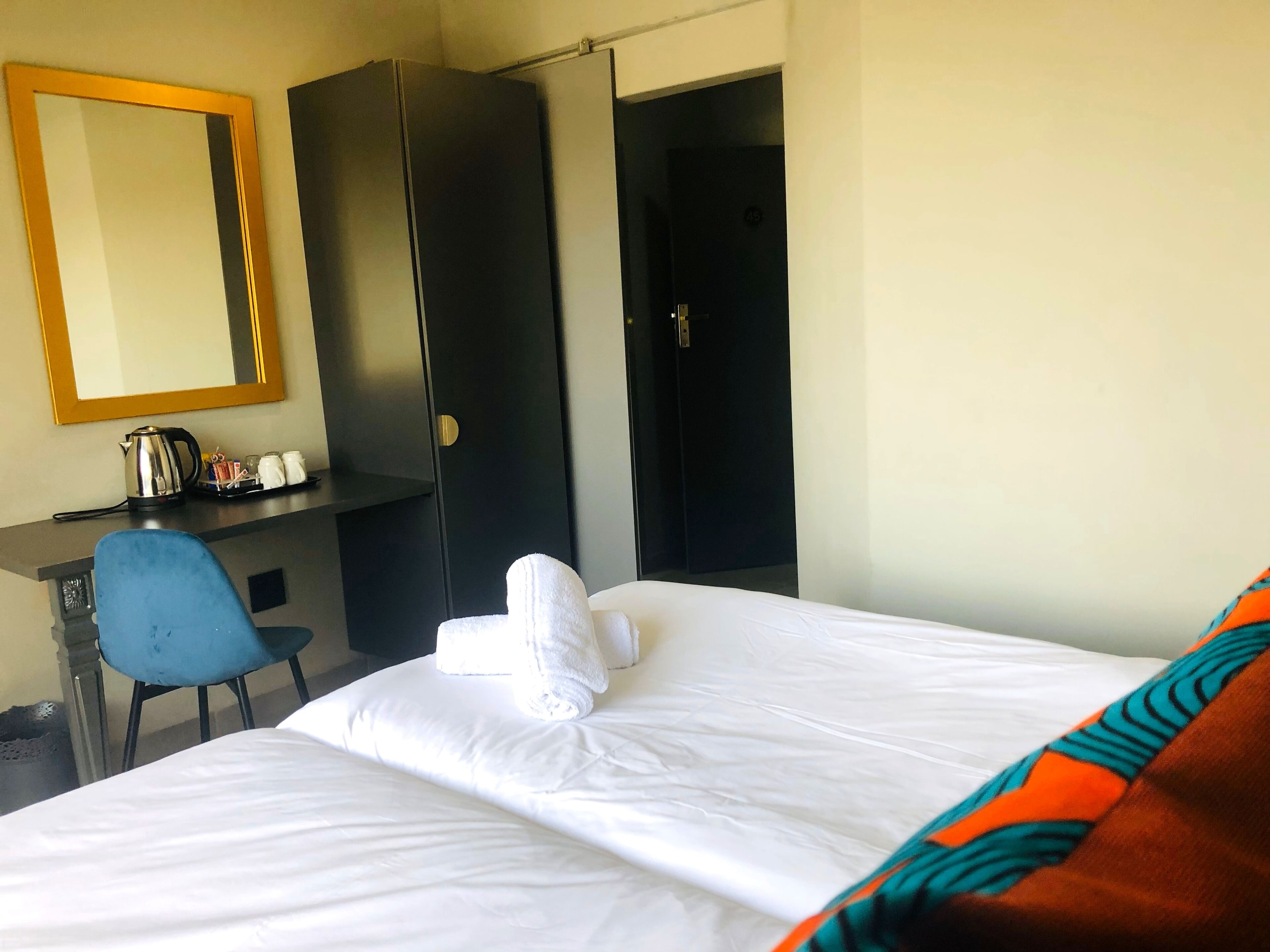 Una habitación de hotel con cama, escritorio, silla, armario y espejo.