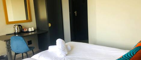 Una habitación de hotel con cama, escritorio, silla, armario y espejo.