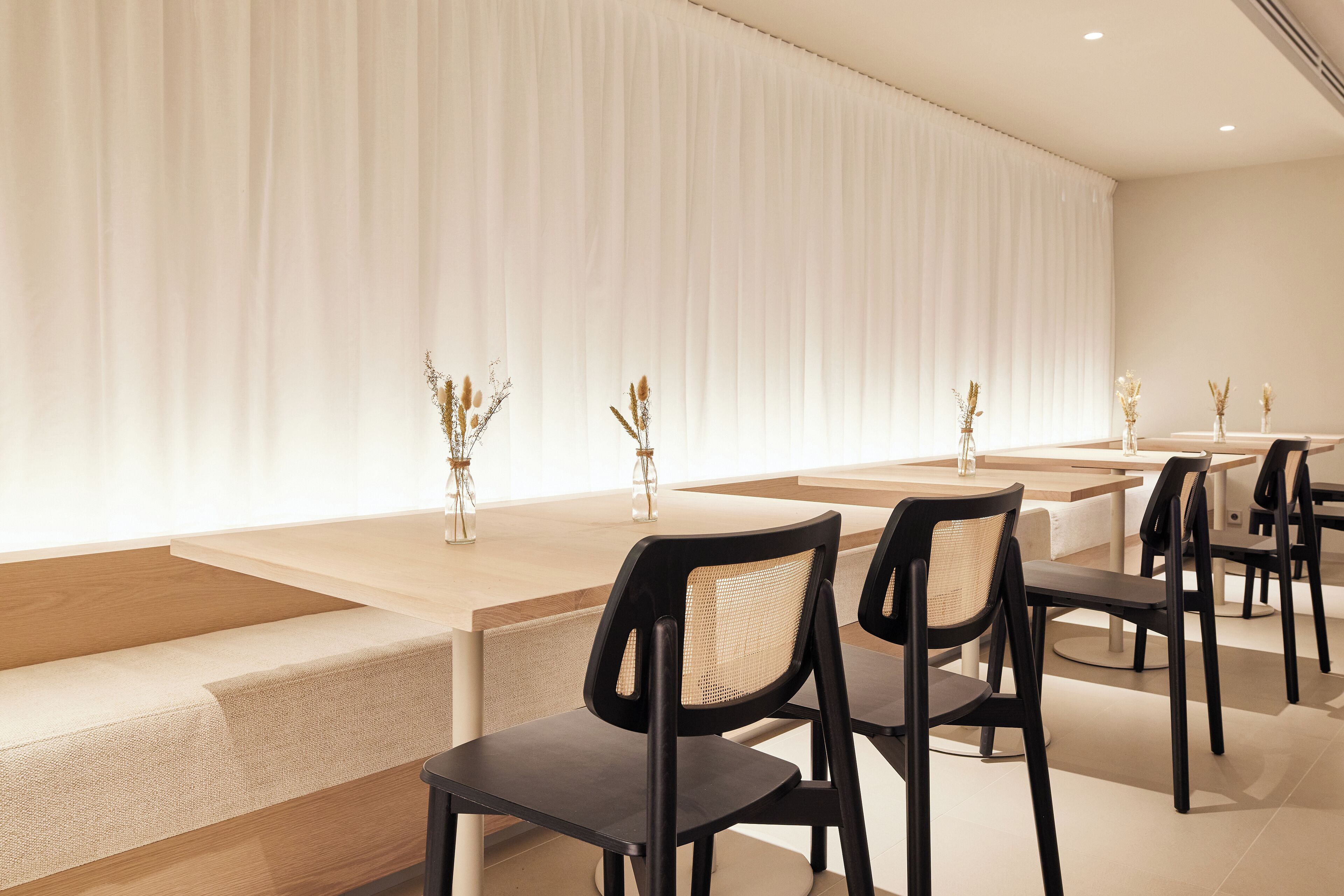 Comedor moderno con mesas largas y sillas negras, con una paleta de colores neutros y decoración sencilla.