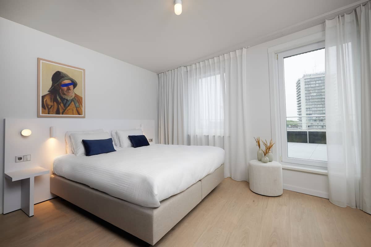 Un dormitorio moderno con una cama grande, cortinas blancas, una mesita de noche y un cuadro en la pared.
