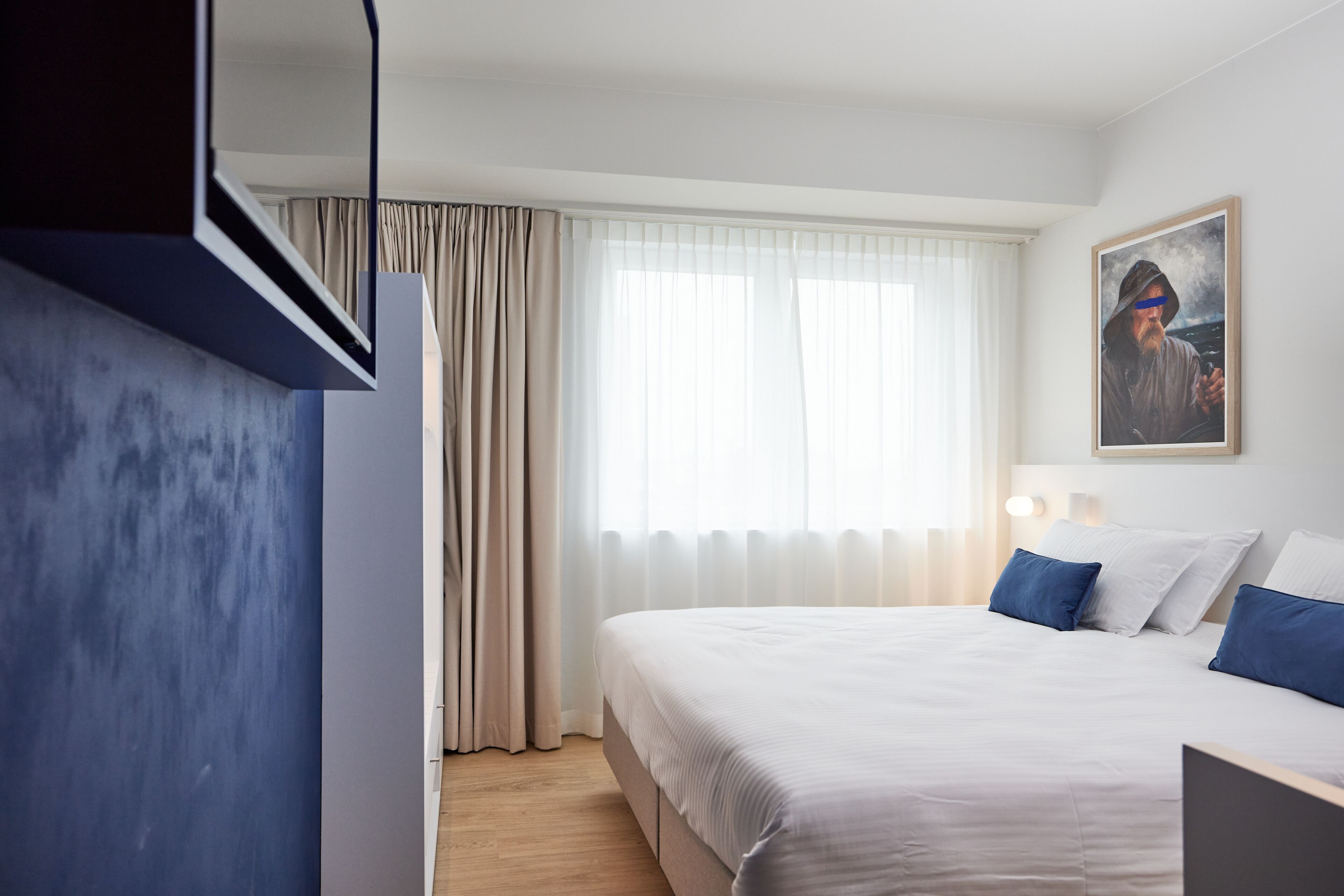 A hotel room with a bed, curtains, a painting, and a bedside table.