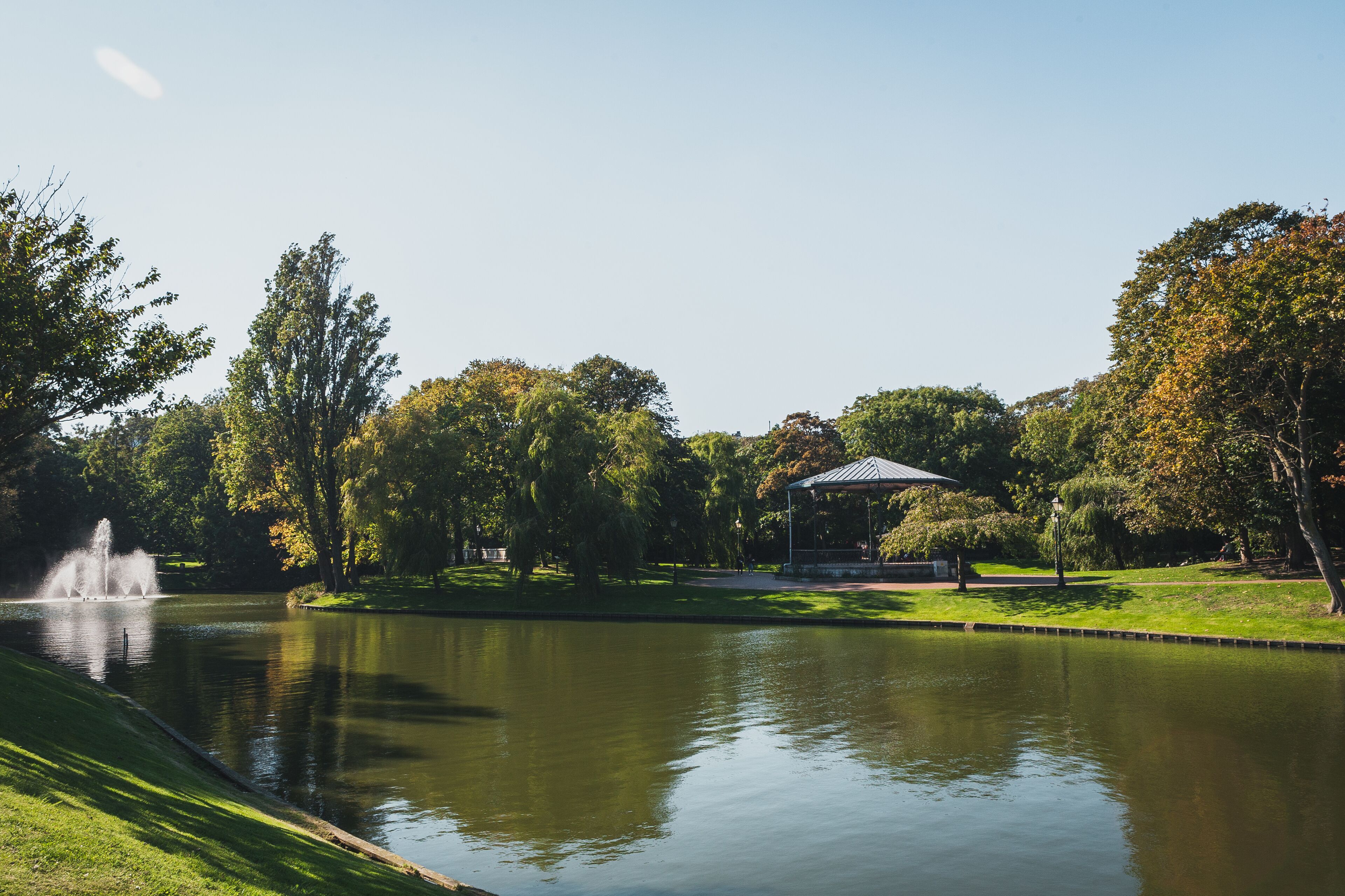 A tranquil park with a pond, a gazebo, and a fountain.