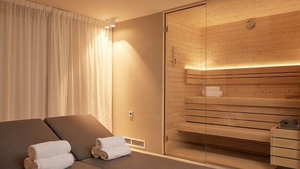 Una habitación de hotel moderna con una cama grande, un box de ducha de vidrio y una zona de sauna de madera.