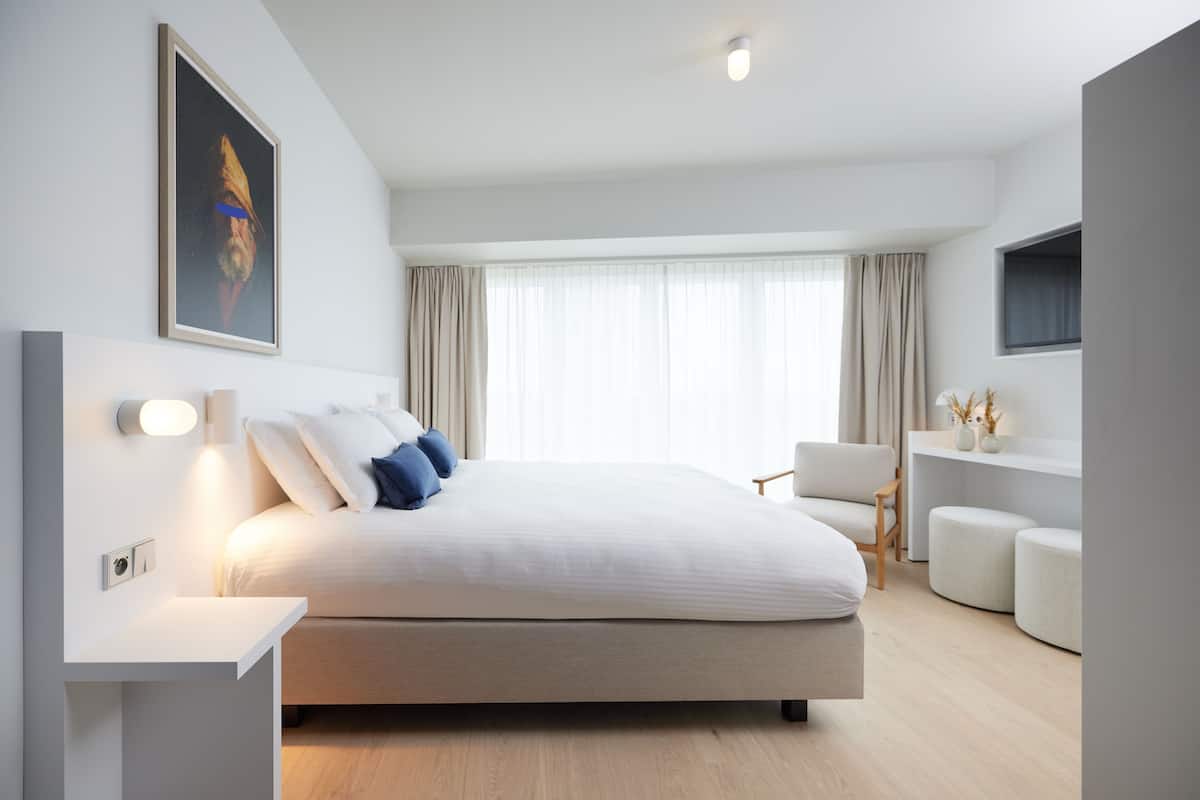 Un dormitorio moderno con una cama grande, una mesita de noche, una silla y un televisor montado en la pared.