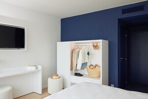 A bedroom with a bed, a wardrobe, a desk, and a television.