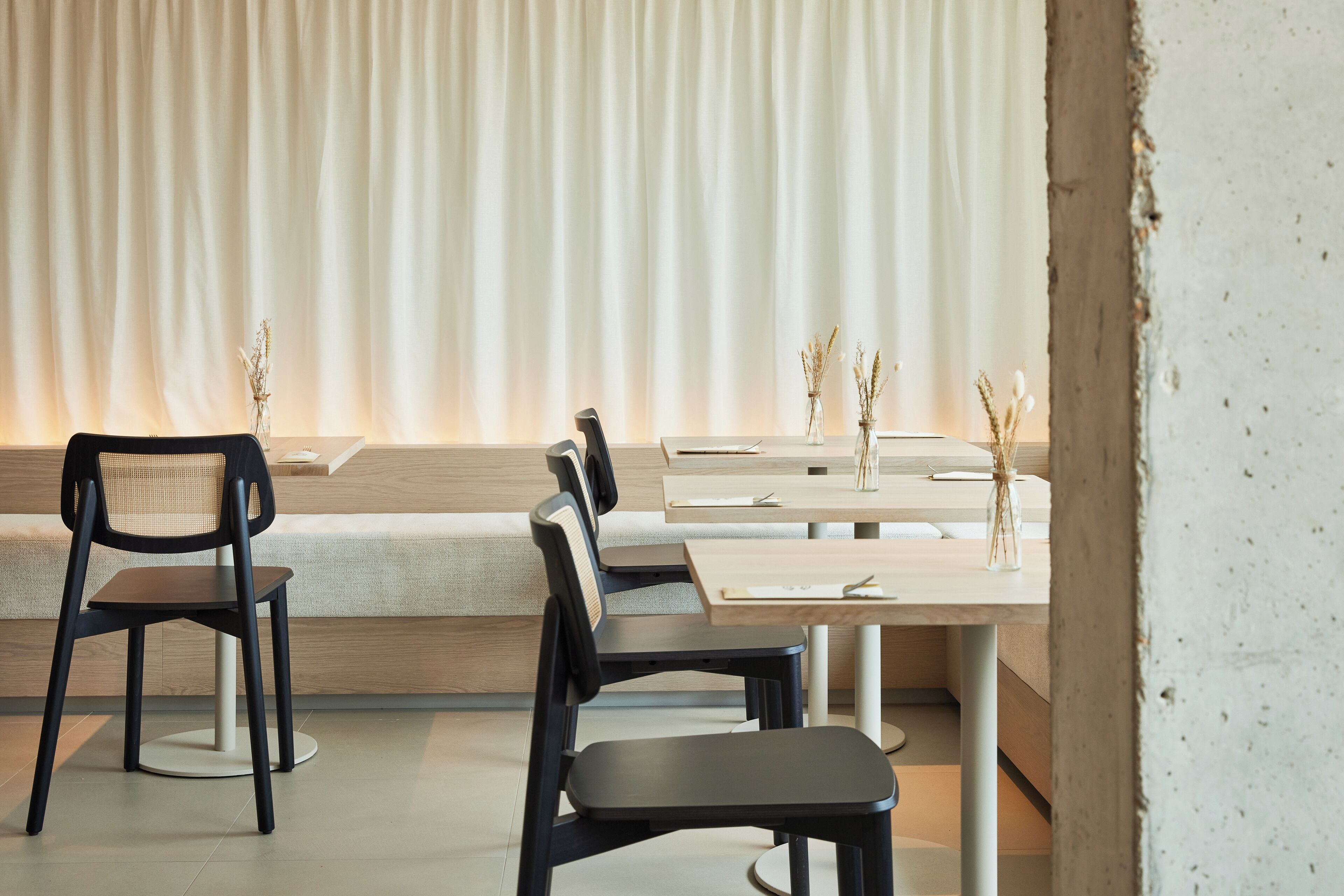 A modern dining area with a long table and chairs, a bench, and a curtain backdrop.