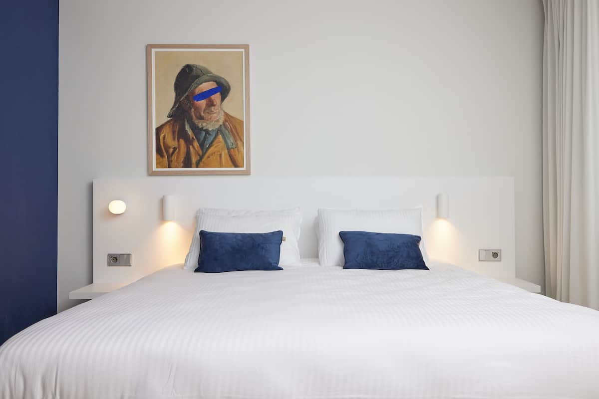 Una cama bien hecha con ropa blanca y dos almohadas azules, un cuadro en la pared y lámparas de noche.