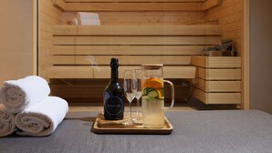 Una sala de sauna con bancos de madera, una botella de Cervezo, dos vasos, y una bandeja con toallas y una jarra de agua.